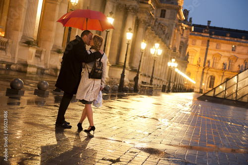 Foto: Caucasian couple kissing in rain at night at the Louvre Caucasian couple kissing in rain at night at the Louvre