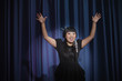 Elegant Asian woman singing into microphone with arms raised