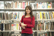 Smiling Hispanic woman holding book in library