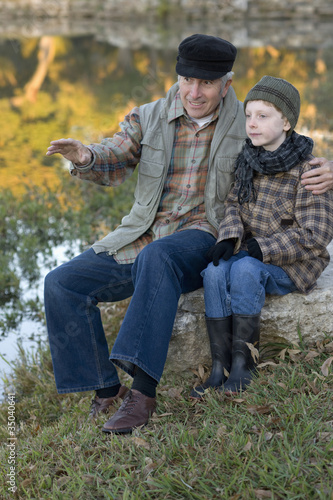 Photo: Caucasian grandfather sitting near lake with grandson Caucasian grandfather sitting near lake with grandson