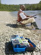 Black man with tackle box fishing in stream