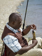 Black man removing fish from hook near stream