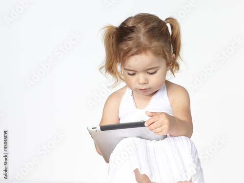 Photo: Cute little girl is playing concentrated with touchpad Cute little girl is playing concentrated with touchpad