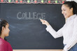 Girl watching teacher write the word “college” on blackboard