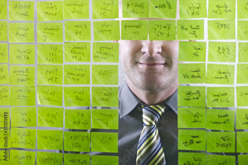 Photo: Caucasian businessman looking at adhesive notes on wall Caucasian businessman looking at adhesive notes on wall