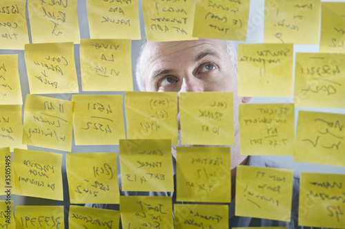 Foto: Caucasian businessman looking at adhesive notes on wall Caucasian businessman looking at adhesive notes on wall