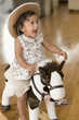 Hispanic girl riding toy horse and wearing cowboy hat