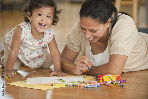 Photo: Hispanic mother laying on floor drawing with daughter Hispanic mother laying on floor drawing with daughter