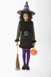 Mixed race girl in Halloween costume holding broom and jack o'lantern