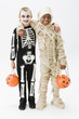 Boys in skeleton and mummy costumes holding jack o'lantern