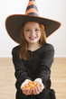 Caucasian girl in witch costume holding Halloween candy
