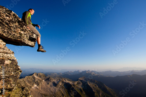 Photo: Young man sitting on rock above mountain range Young man sitting on rock above mountain range