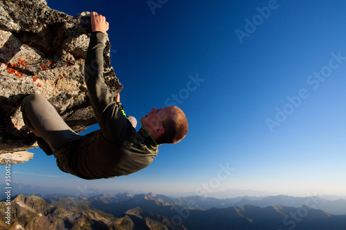 Photo: Young man climbing the rock high above mountain range Young man climbing the rock high above mountain range
