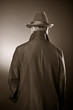 The man in a raincoat and a hat. The rear view