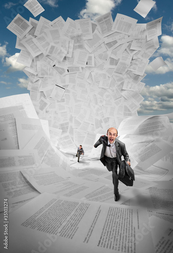 Photo: Businessmen running away from wave of documents Businessmen running away from wave of documents