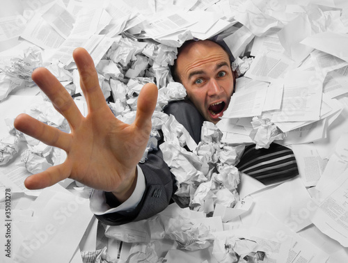 Photo: Businessman sinking in heap of documents Businessman sinking in heap of documents