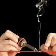 Technician Soldering a Red Wire on a Pure Black Background.