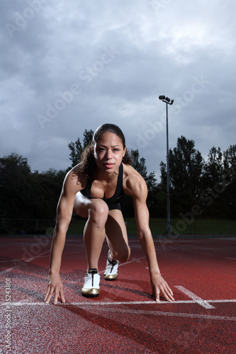 Photo: Female athlete in starting position on track Female athlete in starting position on track