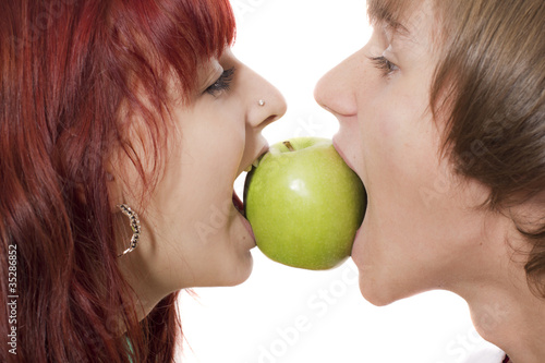 Photo: Close-up of happy couple biting a green apple from another sides Close-up of happy couple biting a green apple from another sides