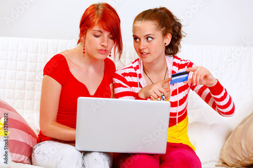 Photo: Two pretty girlfriends shopping in net using credit card Two pretty girlfriends shopping in net using credit card