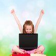 Photo: A young girl with a laptop sitting have joyfully hands up A young girl with a laptop sitting have joyfully hands up