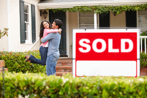 Photo: Hispanic couple outside home with sold sign Hispanic couple outside home with sold sign