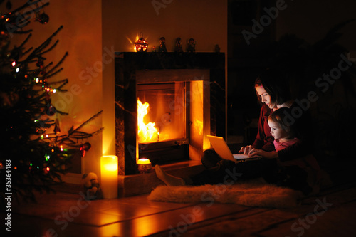 Photo: Young mother and daughter by a fireplace on Christmas Young mother and daughter by a fireplace on Christmas