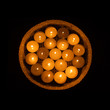 Many burning candles in a brown straw dish isolated on black