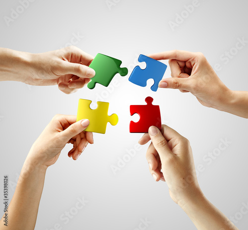 Photo: Hands and puzzle on gray background. Teamwork solving a puzzle Hands and puzzle on gray background. Teamwork solving a puzzle