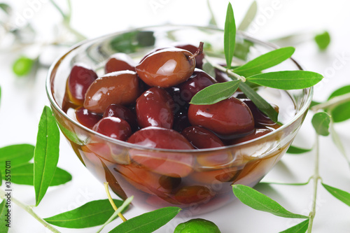 Photo: Black olives in olive oil and fresh leaves in close-up Black olives in olive oil and fresh leaves in close-up