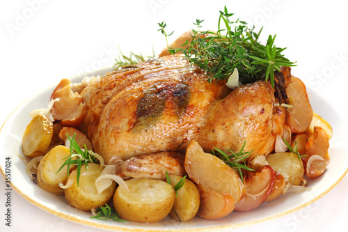 Photo: Whole roasted chicken with potatoes and herbs on white plate Whole roasted chicken with potatoes and herbs on white plate