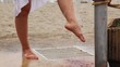 Woman washes feet from sand under water stream on beach
