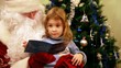 Girl sitting in Santa Claus kneeling in front of tree