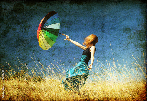 Photo: Redhead girl with umbrella at windy grass meadow. Redhead girl with umbrella at windy grass meadow.