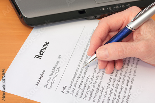 Photo: Hand with Pen Proofreading a Resume by Laptop Hand with Pen Proofreading a Resume by Laptop
