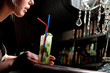 A young blond girl drinking coctail mohito with a straw in a caf
