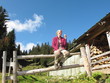 Frau mit lila Jacke sitzt auf Zaun