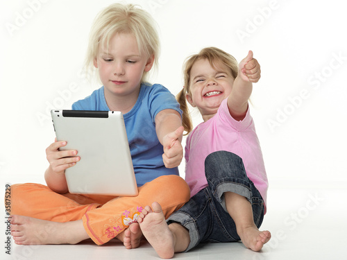 Photo: Adorable little girls seated on the floor playing with touchpad Adorable little girls seated on the floor playing with touchpad