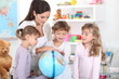a woman and three little girls watching a globe