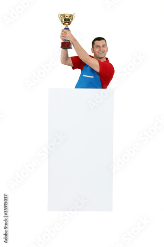 Photo: Man standing behind a blank sign and holding a trophy Man standing behind a blank sign and holding a trophy