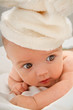Little baby lying on the blanket and is wearing a white hat.