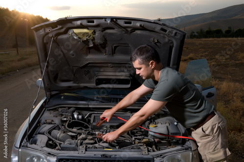 Photo: Adult man using jumper cables to start a car battery. Adult man using jumper cables to start a car battery.