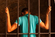 Man with hands tied with rope behind the bars