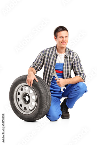 Photo: A male mechanic posing with a spare tire and holding a wrench A male mechanic posing with a spare tire and holding a wrench
