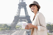 Foto: Woman holding a guide book with the Eiffel Tower in the background, Paris, Ile-de-France, France Woman holding a guide book with the Eiffel Tower in the background, Paris, Ile-de-France, France