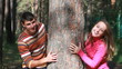 Young couple hiding behind tree trunk and smiling