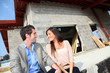 Happy couple sitting in front of house under construction