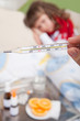 Clinical thermometer in hand showing fever and little sick girl
