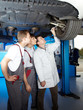 Three motor mechanics controlling a car on a hydraulic lift