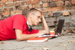 male student working on laptop, lying near the wall